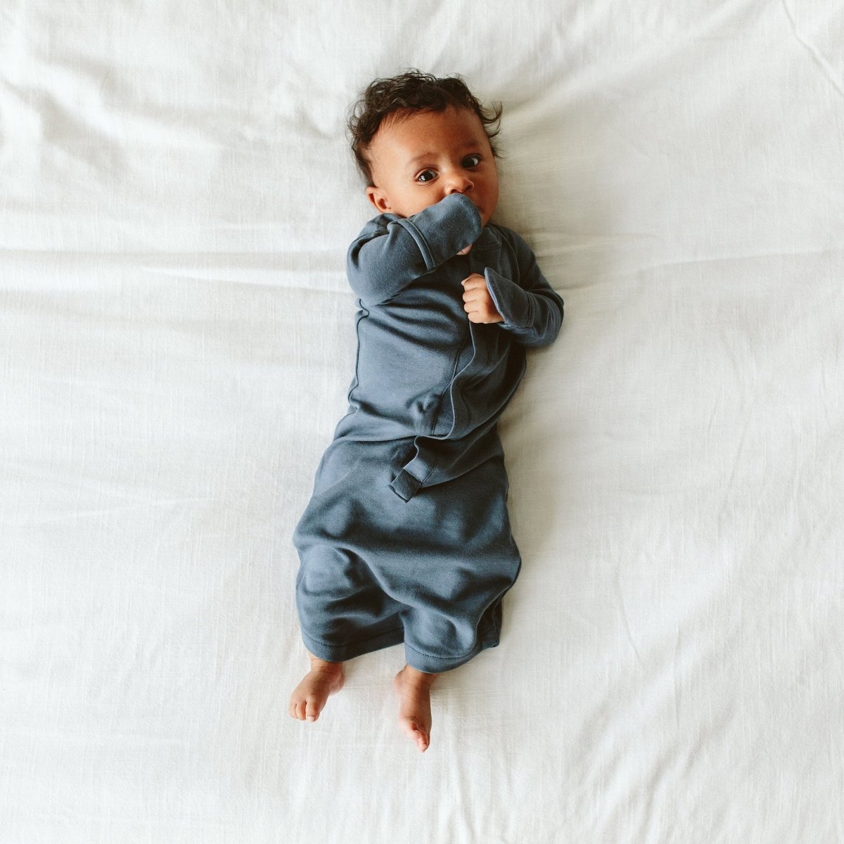 Baby in a blue onesie lying on a white surface