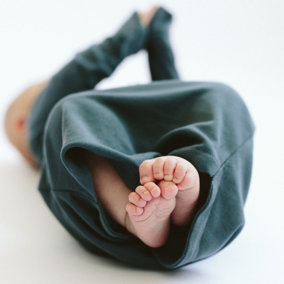 Baby's feet peeking out from under a green blanket on a white background