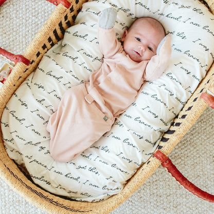 Newborn baby swaddled in a pink blanket with bunny ears in a basket with a text pattern