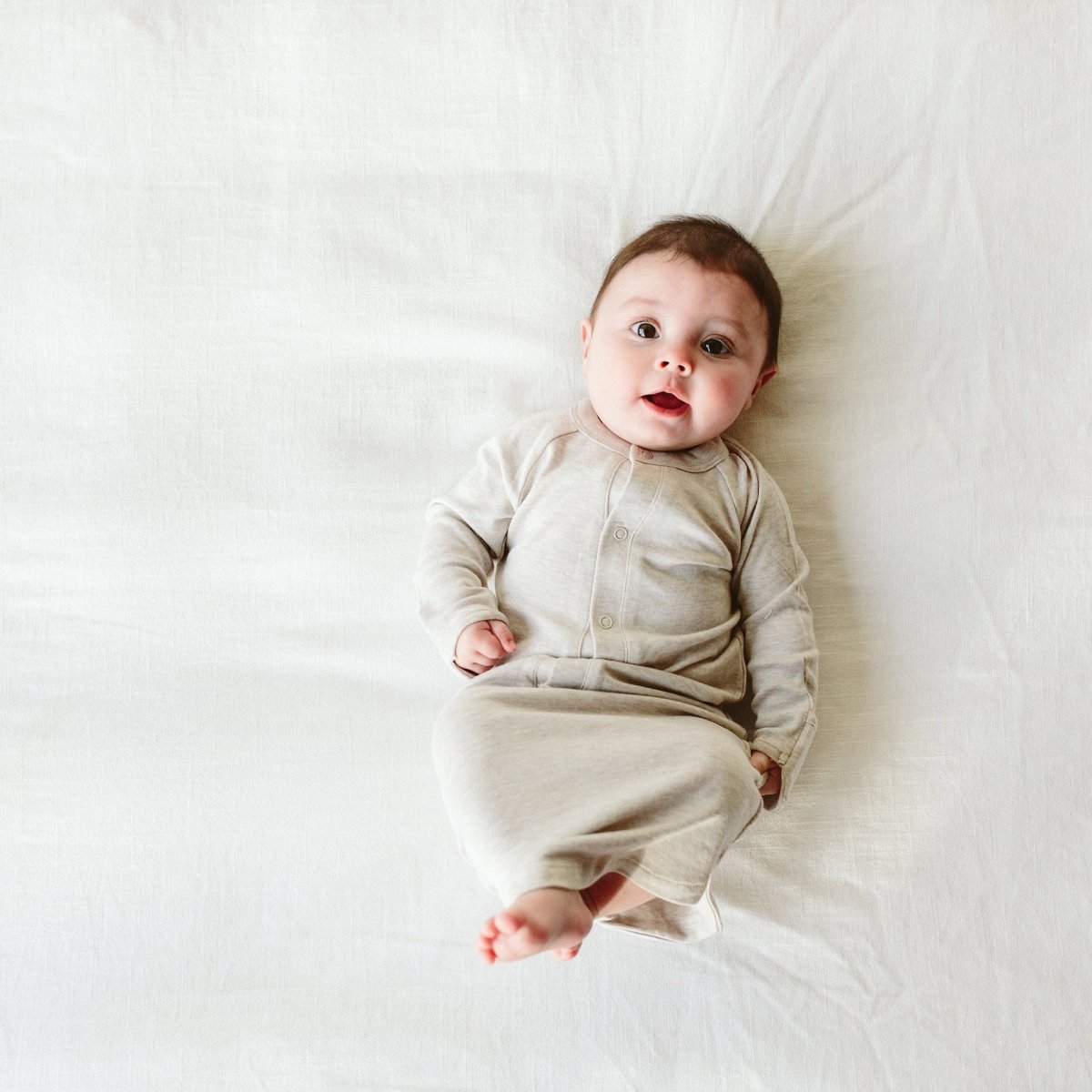 Baby lying on a white bed wearing a beige onesie.