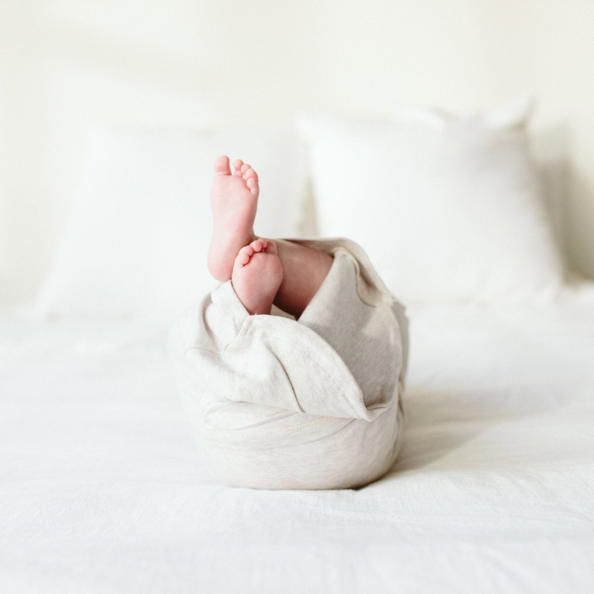 Baby wrapped in a light blanket with feet peeking out on a white background