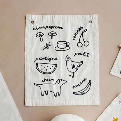 White fabric wall hanging with black line drawings and text on a beige background