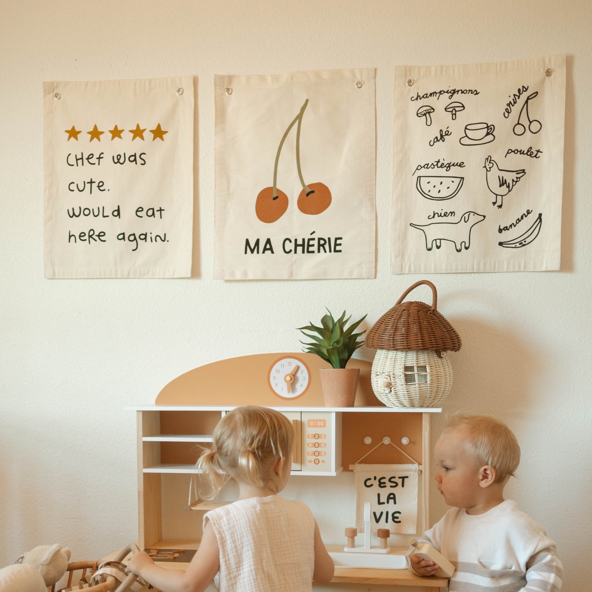 Two children playing with a toy kitchen set in a room with wall decorations.