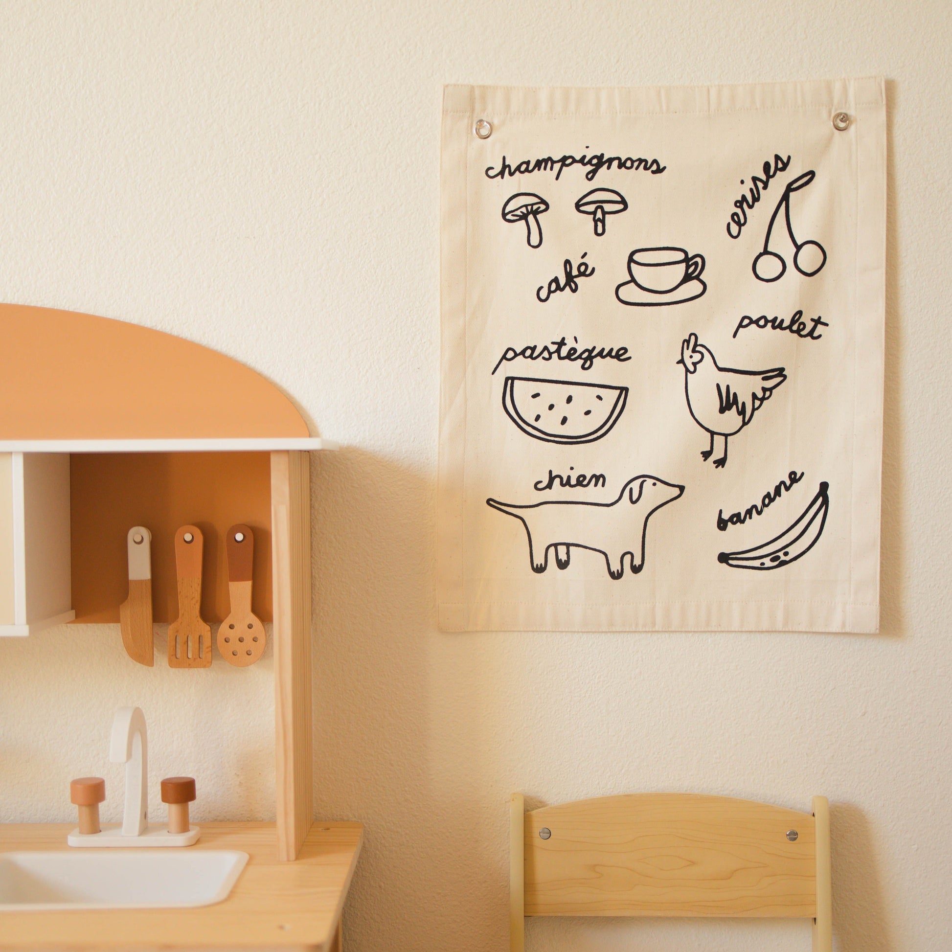 Children's play kitchen with a wall hanging featuring illustrations and text.