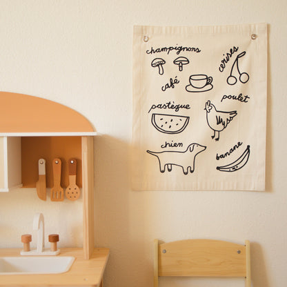 Children's play kitchen with a wall hanging featuring illustrations and text.