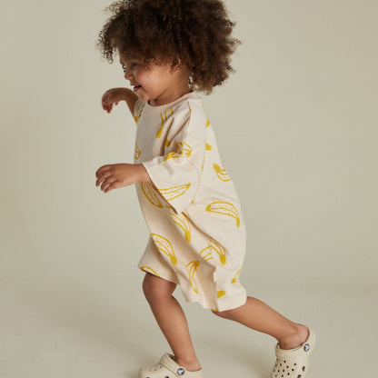 Child wearing a white onesie with yellow banana patterns on a neutral background