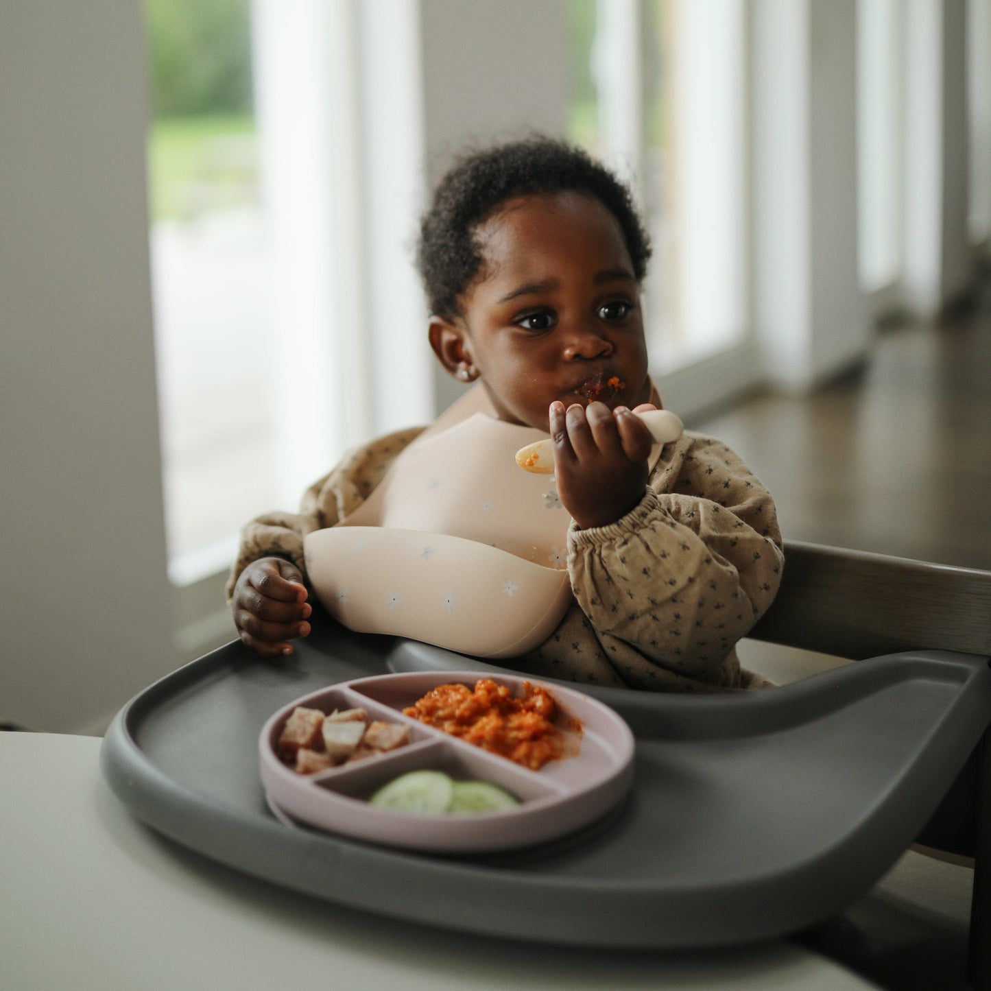 Child sitting in a high chair eating from a tray with food.
