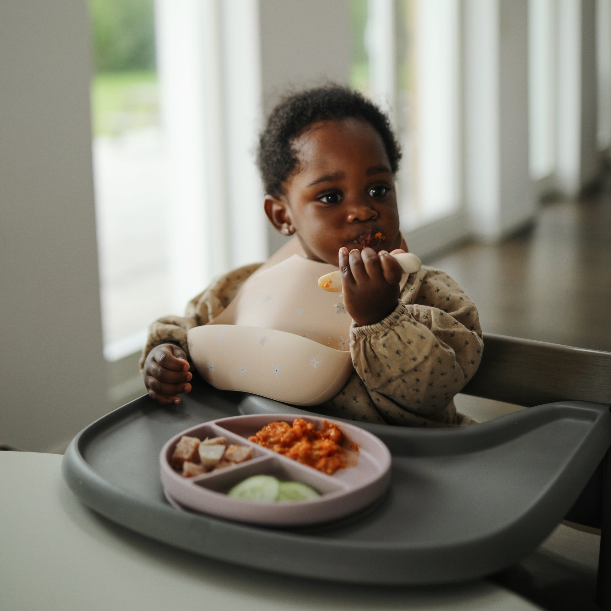 Child sitting in a high chair eating from a tray with food.