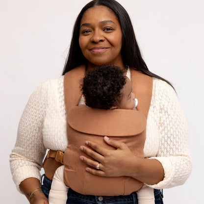 Woman holding a baby in a brown baby carrier against a white background