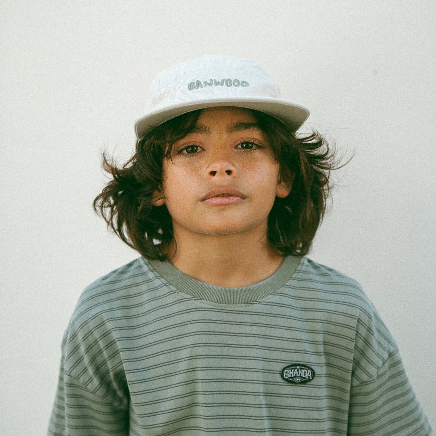 Child wearing a striped shirt and cap with 'Banwood' branding against a plain background