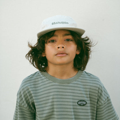 Child wearing a striped shirt and cap with 'Banwood' branding against a plain background