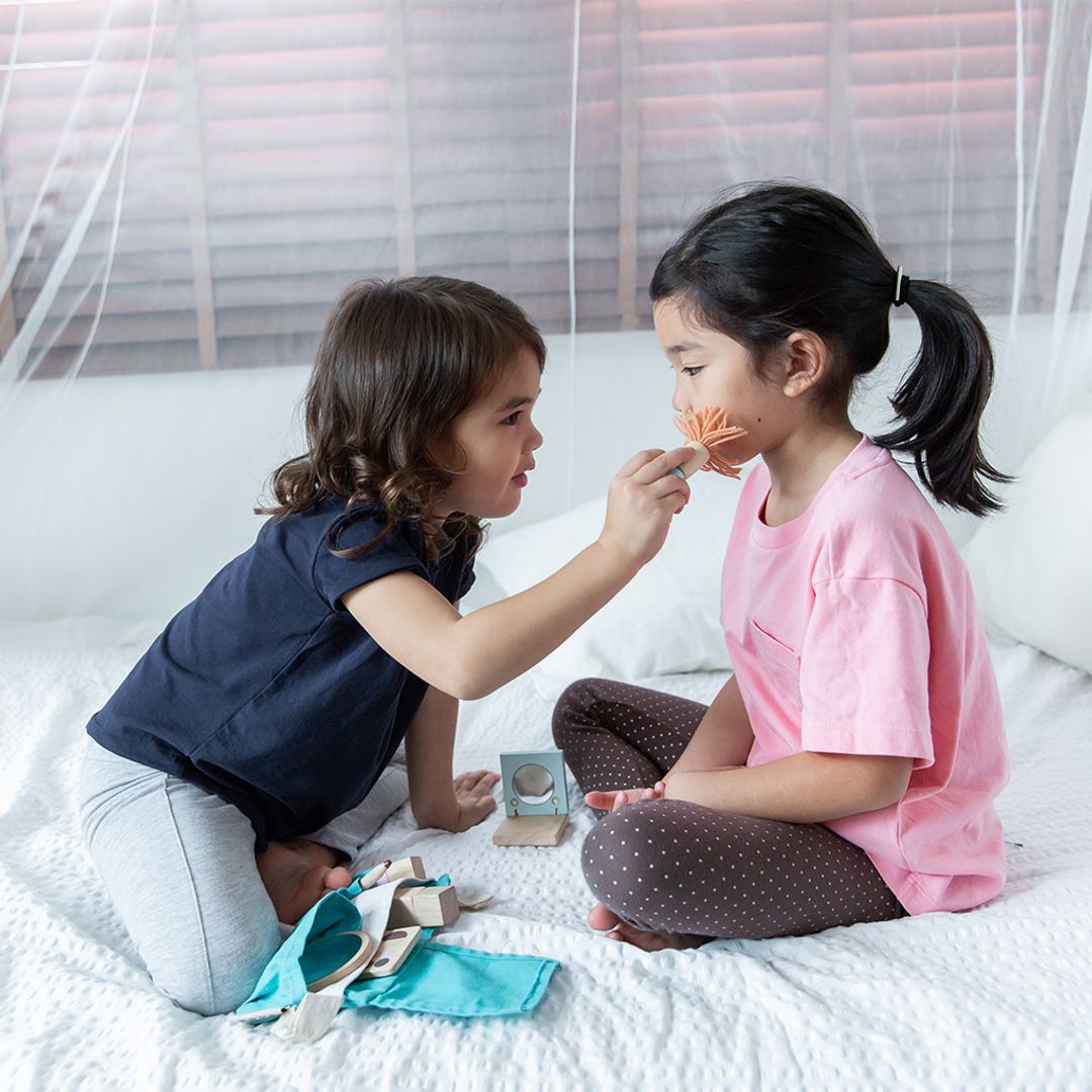 Two young girls playing with makeup on a bed.