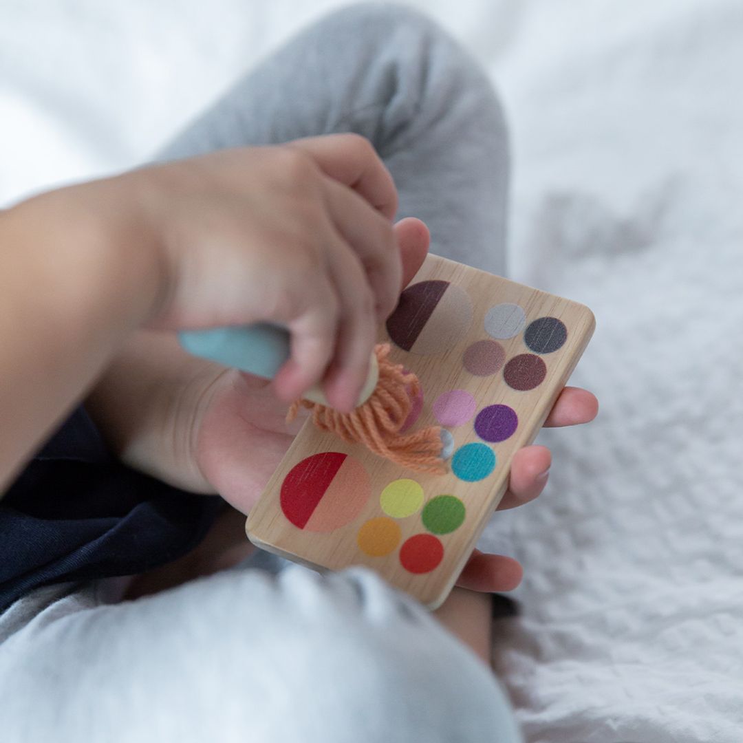 Child's hand holding a wooden color swatch card with paintbrush