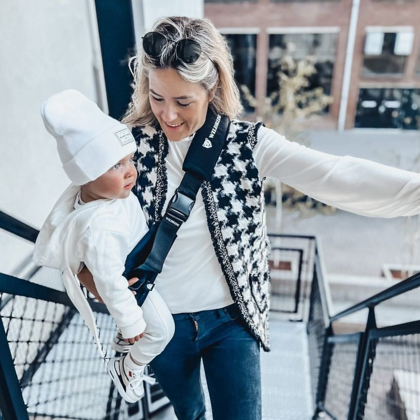 Woman holding a child in a baby carrier on a snowy day.