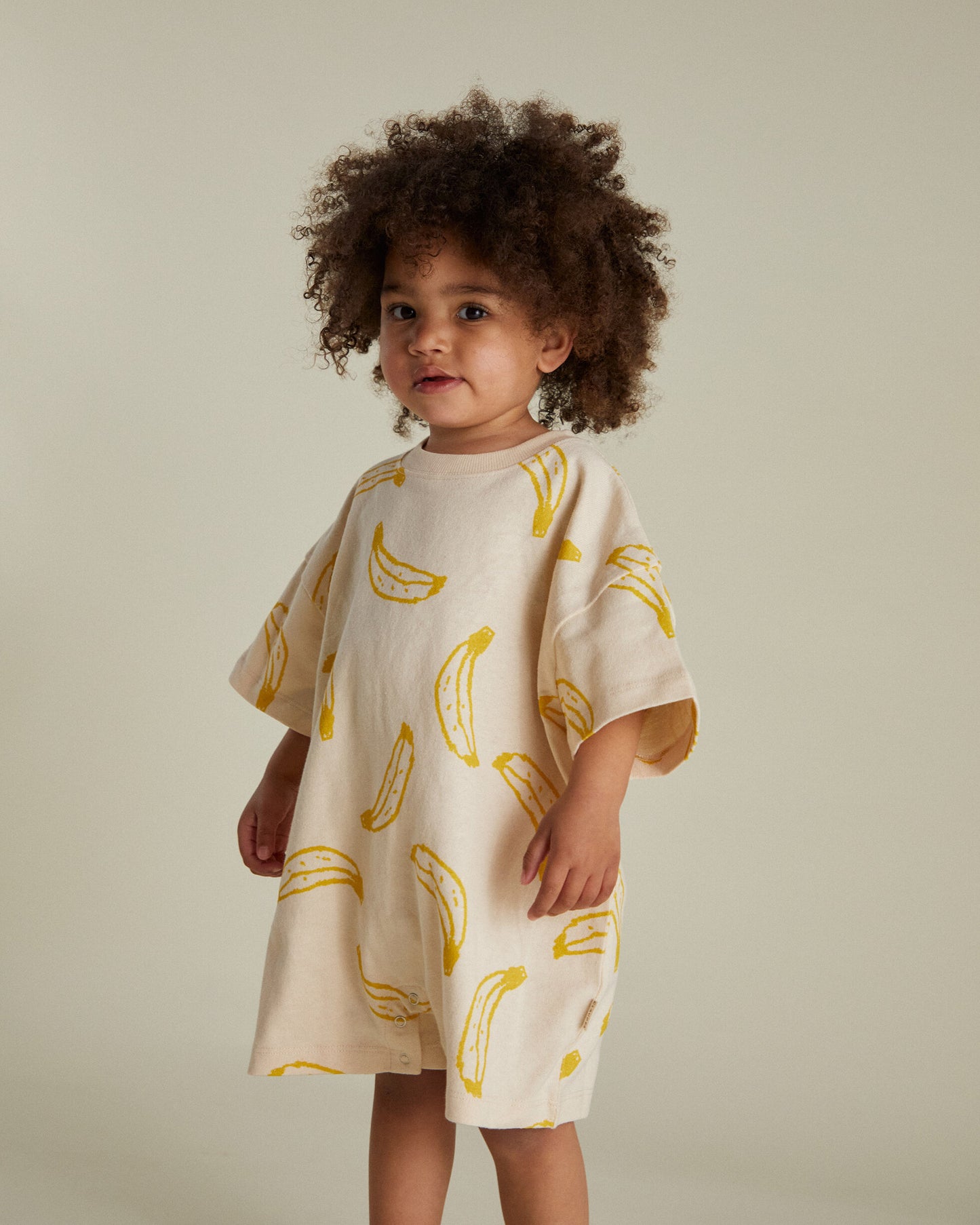 Child wearing a cream dress with yellow banana prints against a neutral background