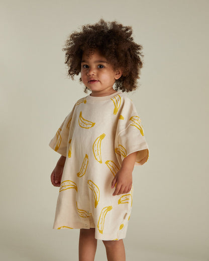 Child wearing a cream dress with yellow banana prints against a neutral background