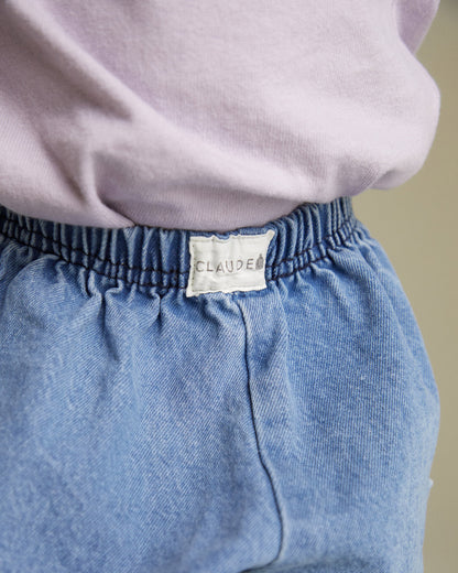 Blue denim pants with a visible brand label on a neutral background