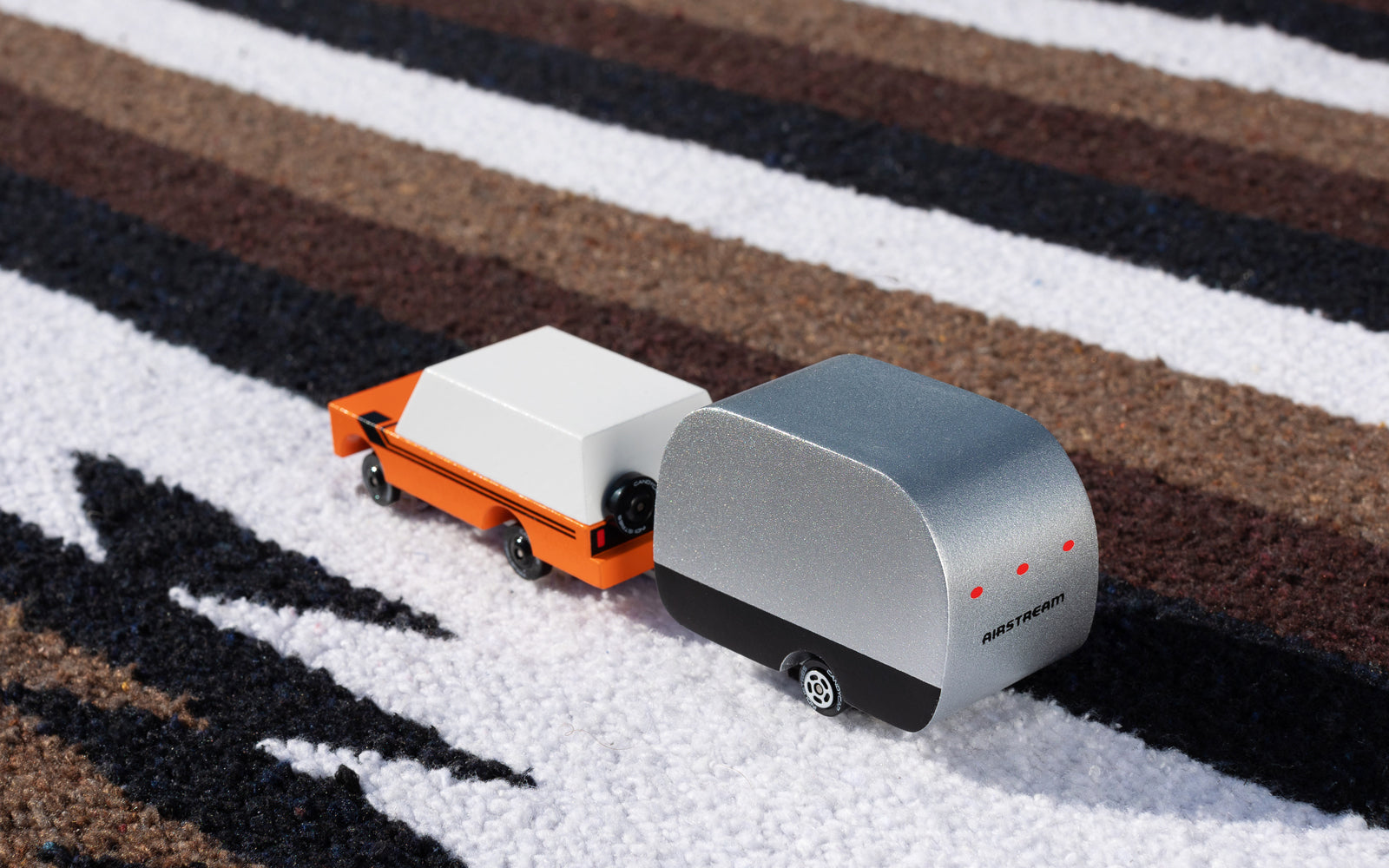 Two toy cars on a striped carpet, one orange and white, the other gray with black wheels.