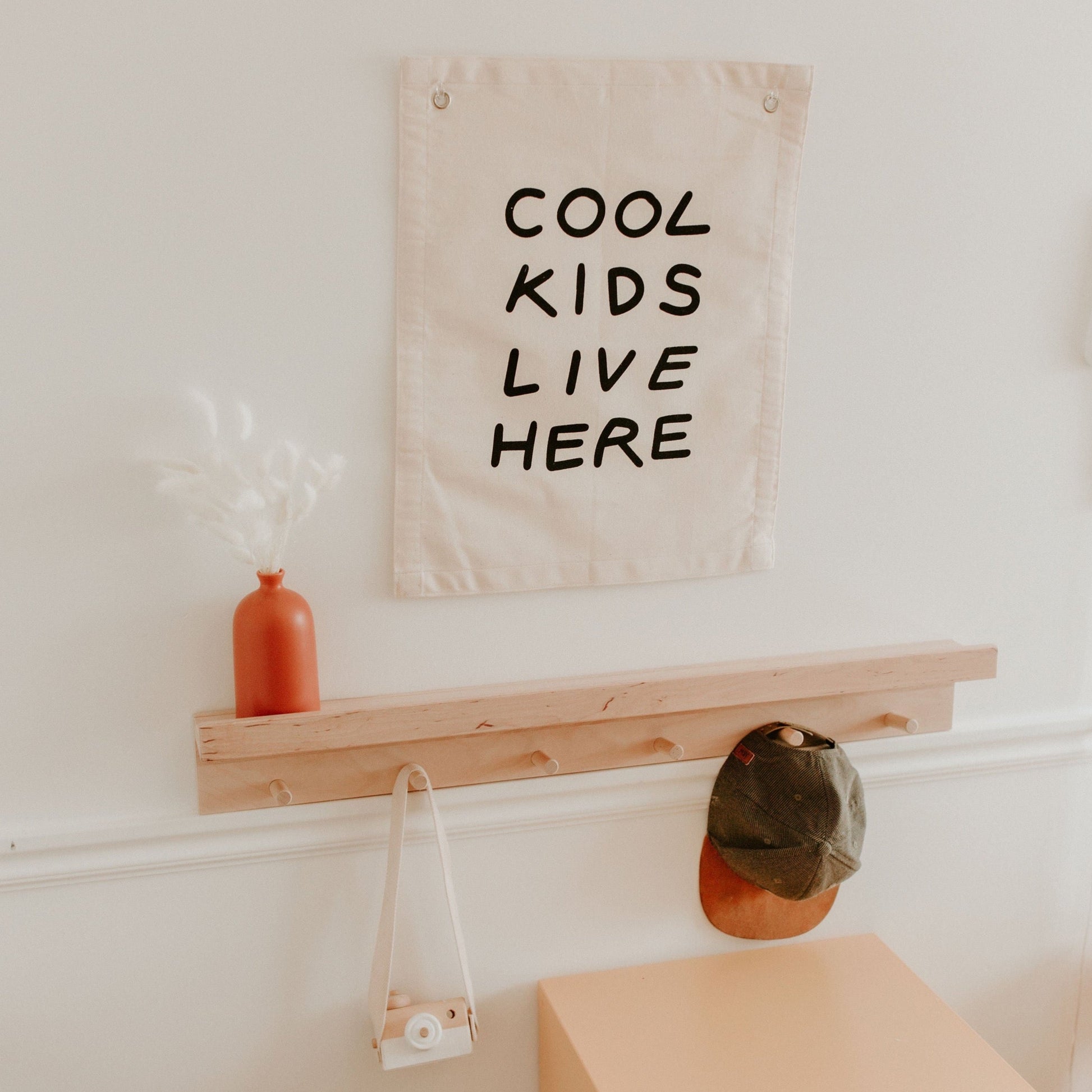 Wall with a sign reading 'Cool Kids Live Here', a wooden shelf, and a vase.