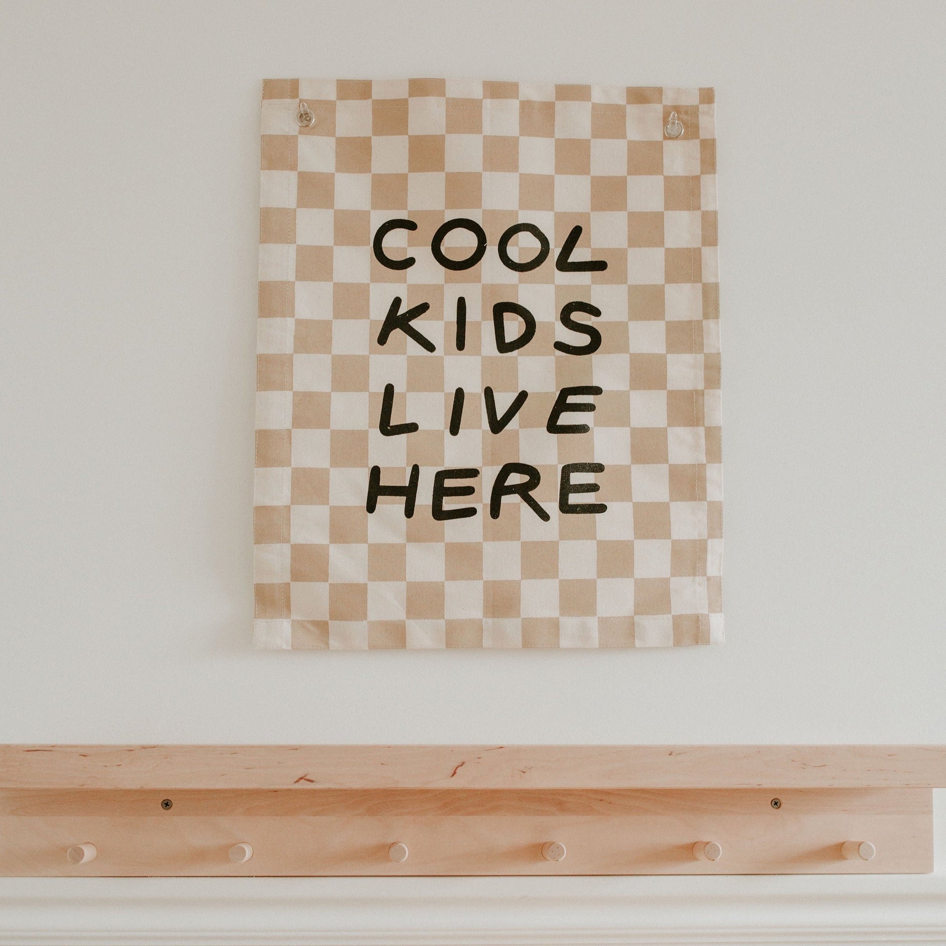 Checkered wall art with 'Cool Kids Live Here' text on a white wall above a wooden shelf.