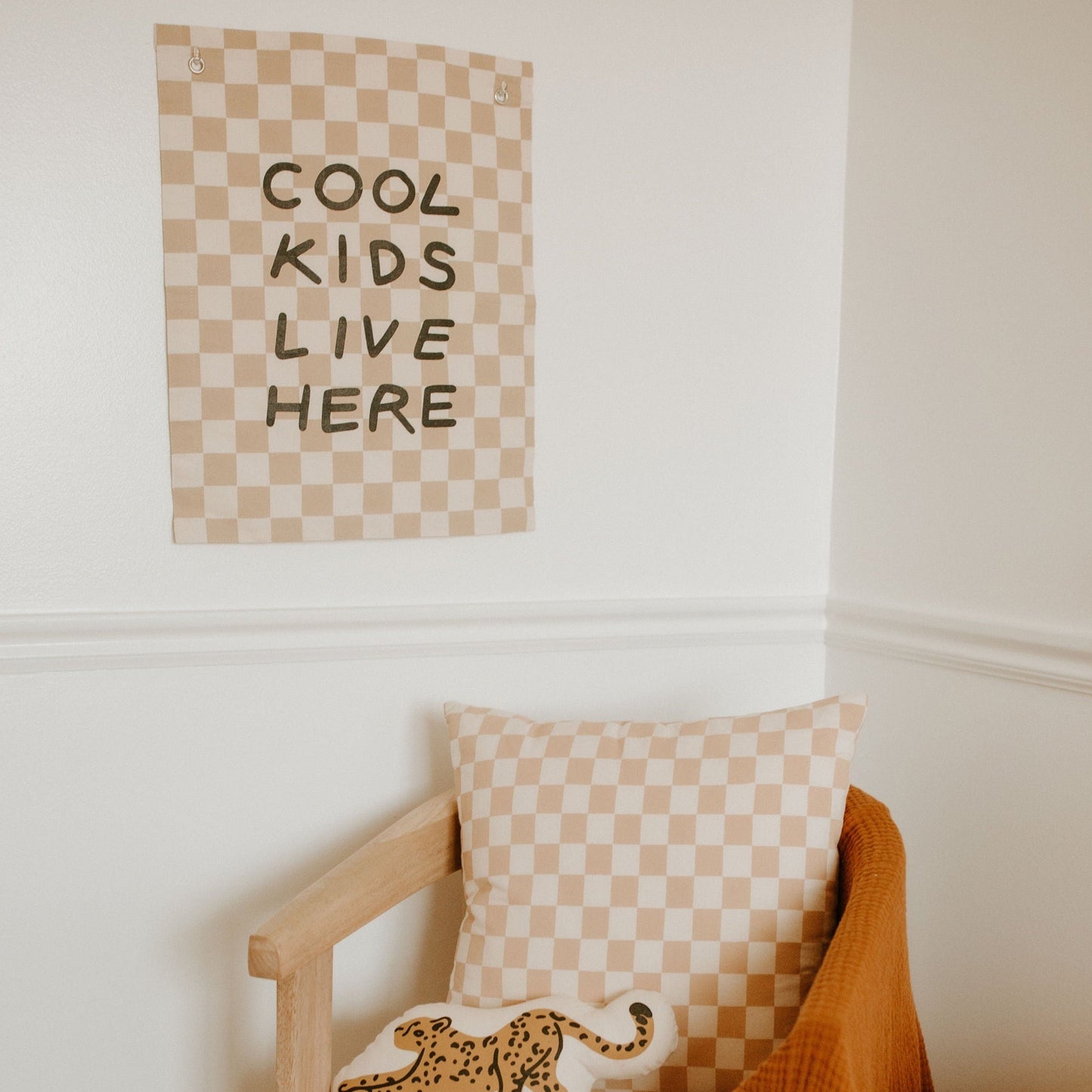 Checkered poster with 'Cool Kids Live Here' text on a wall above a wooden chair with a leopard print pillow.