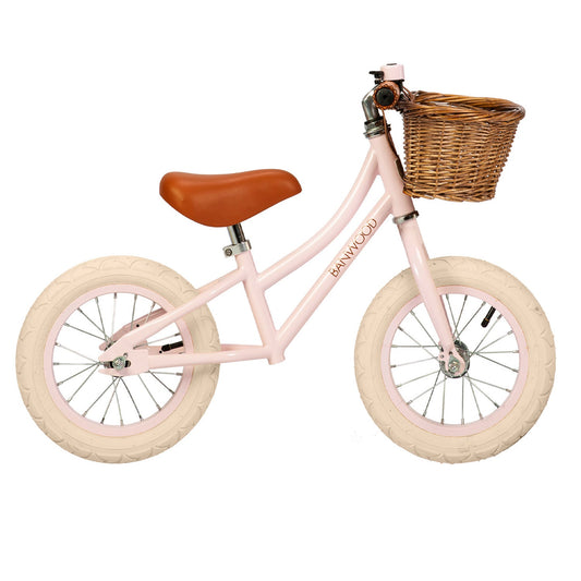 Pink balance bike with a brown basket and seat on a white background