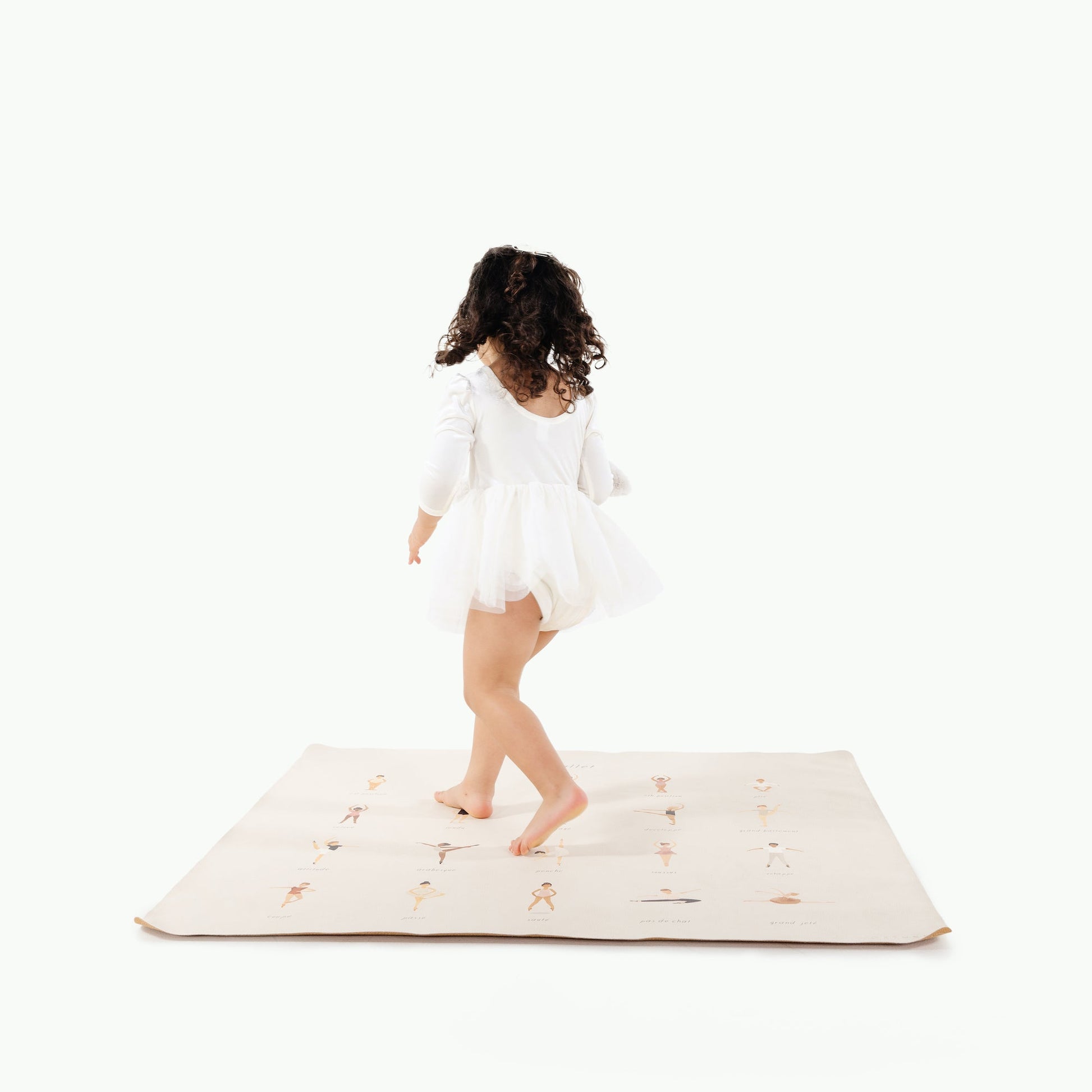 Child in a white dress standing on a white mat with a white background