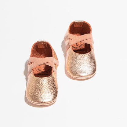 Pair of rose gold baby shoes with pink straps on a white background