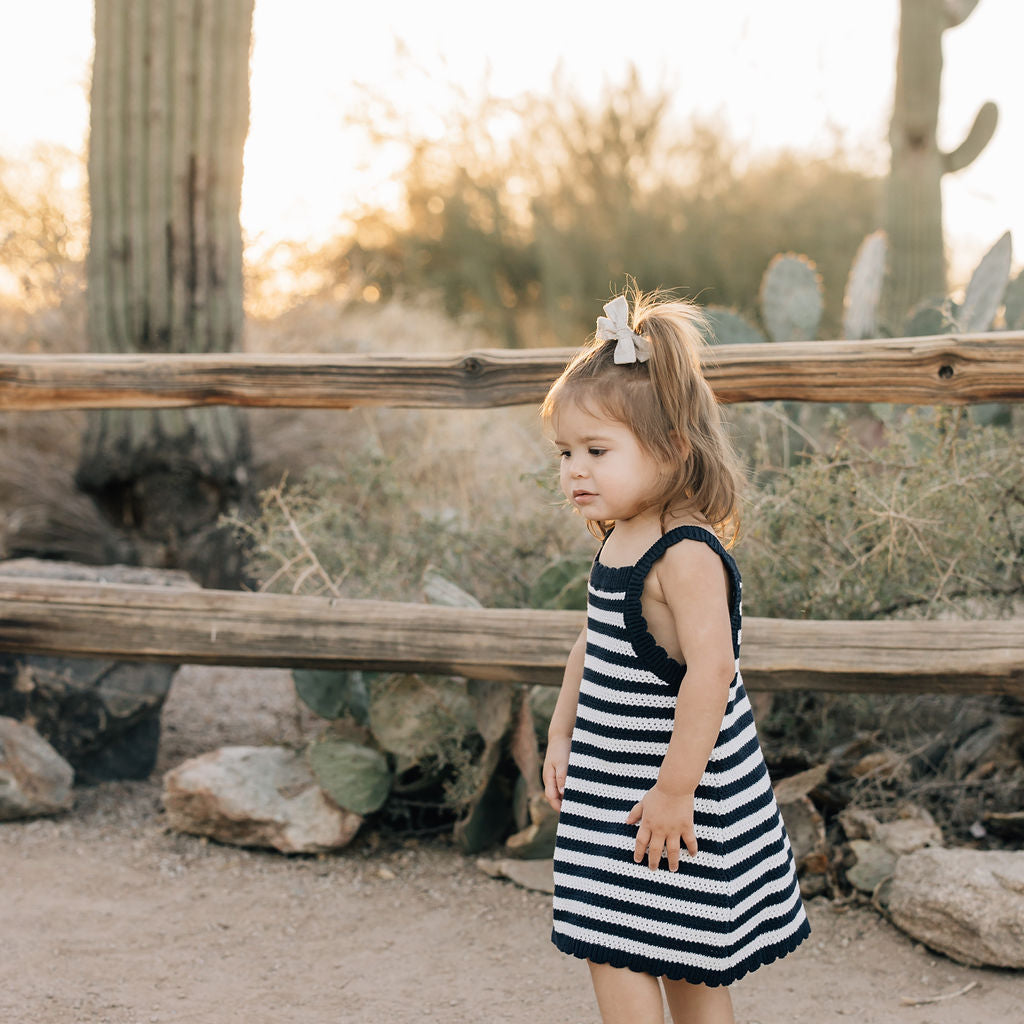 Young girl in a black and white striped dress standing in a desert landscape with cacti.