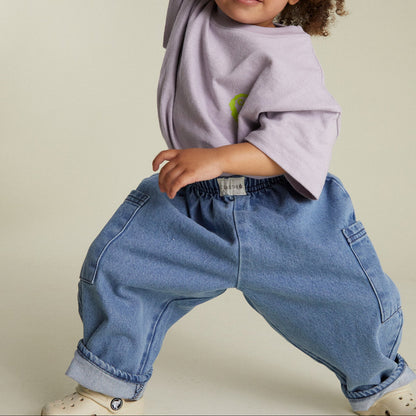 Child wearing a light purple shirt and blue jeans on a beige background