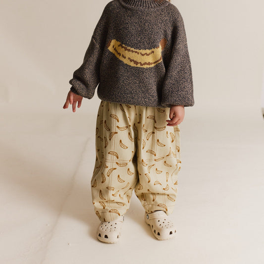 Child wearing a sweater with banana on the chest and trousers with an all over banana print.