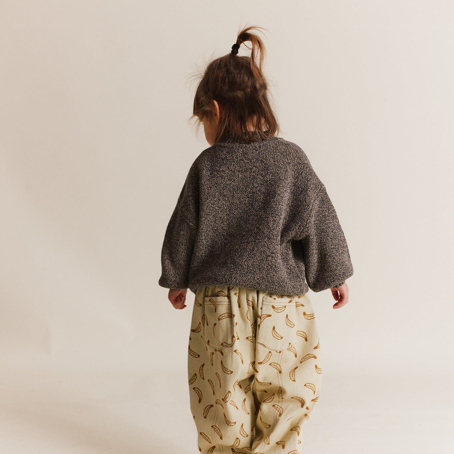 Child wearing a textured gray sweater and banana-patterned pants on a plain background