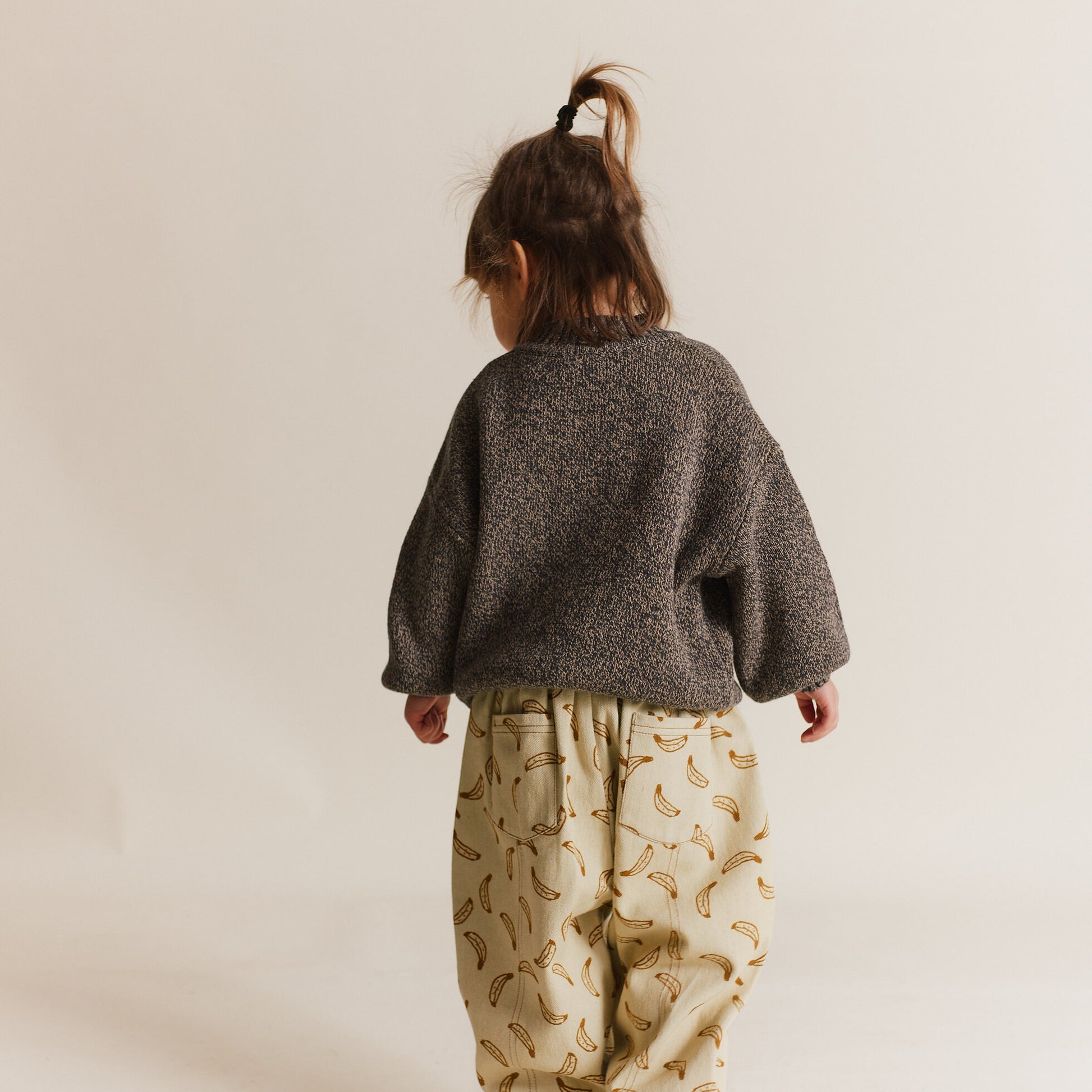 Child wearing a textured gray sweater and banana-patterned pants on a plain background