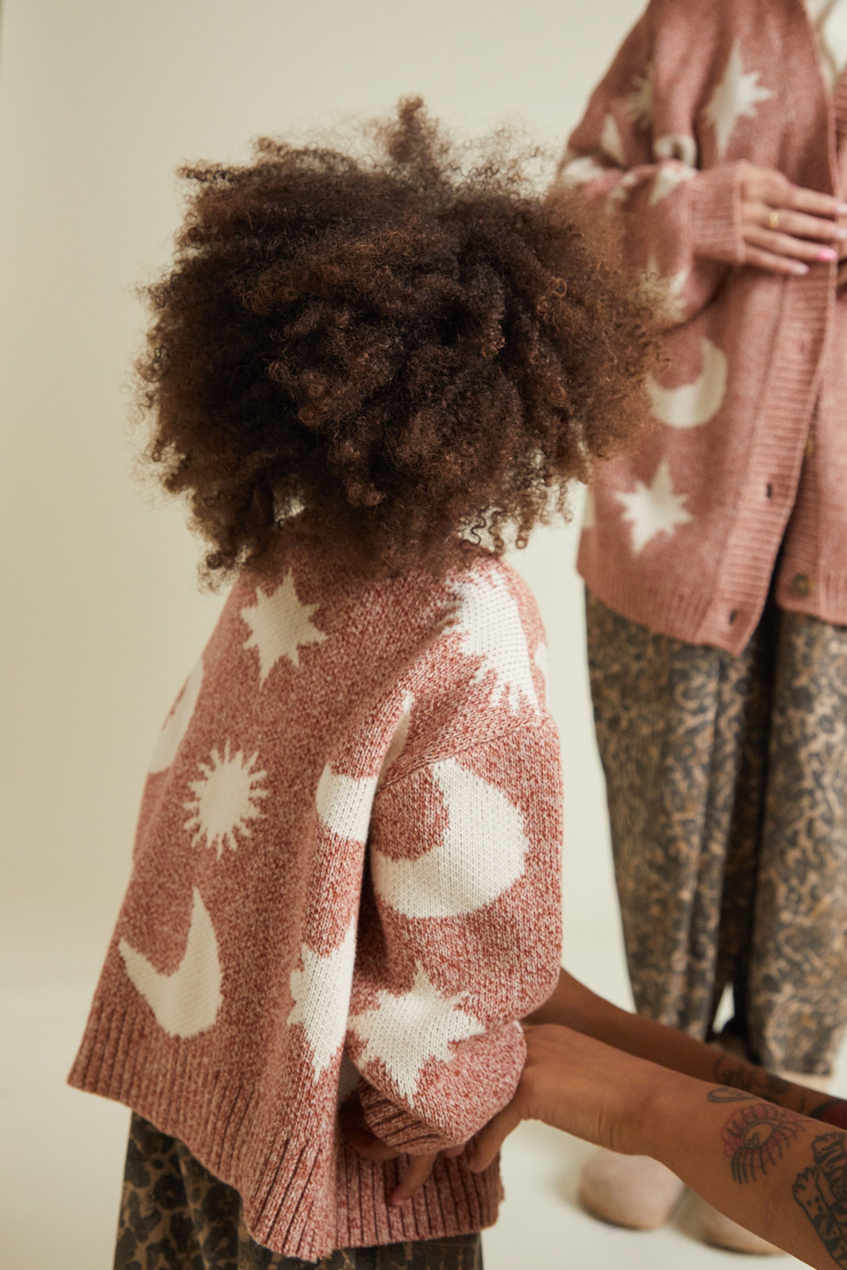 Two people wearing pink cardigans with star and moon patterns against a neutral background.