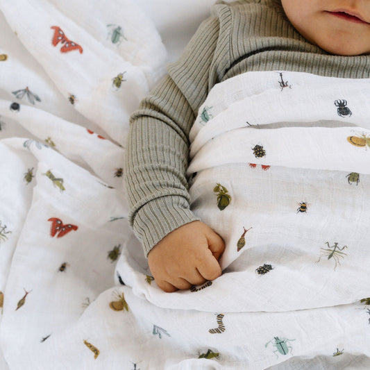 Child wrapped in a white blanket with small colorful patterns, wearing a green sweater.