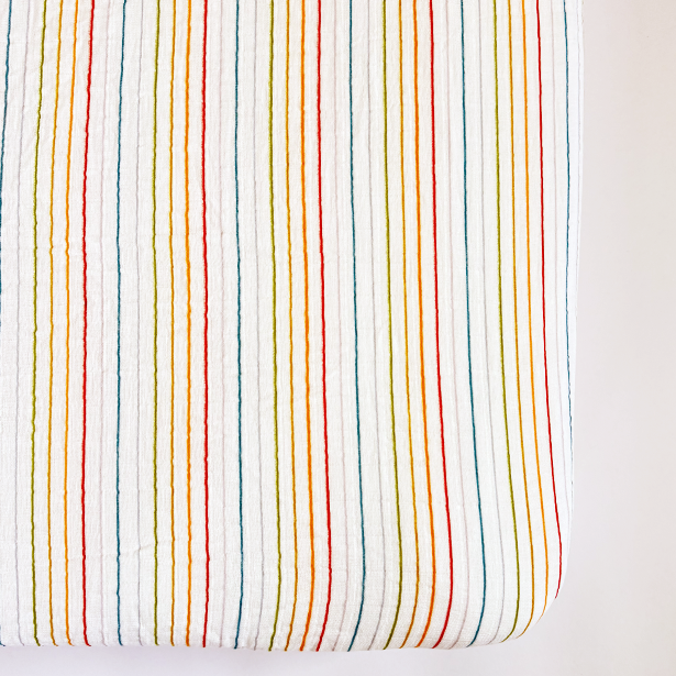 Fitted crib sheet with multicolored stripes on a white background