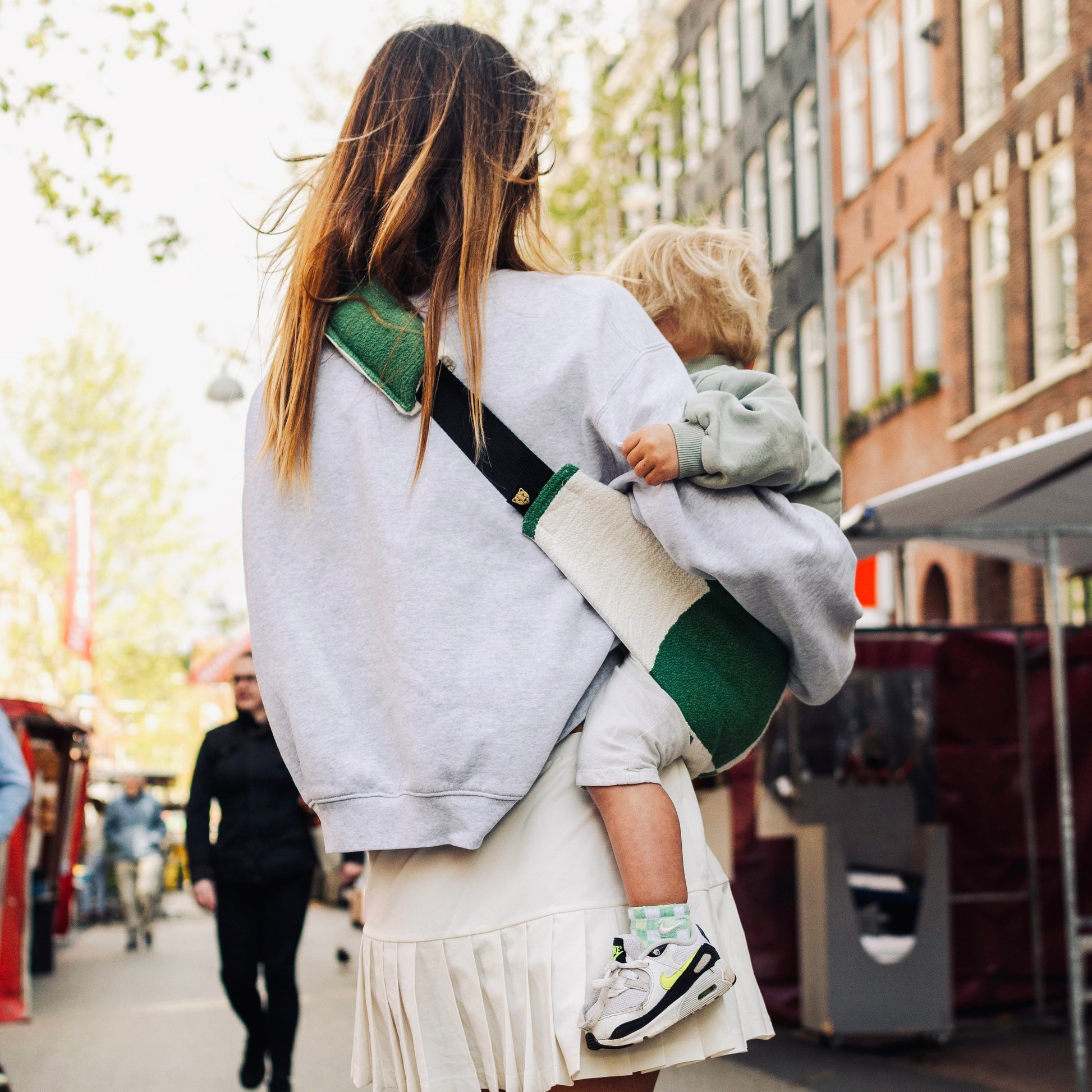 Woman carrying a child on a city street with buildings and people in the background