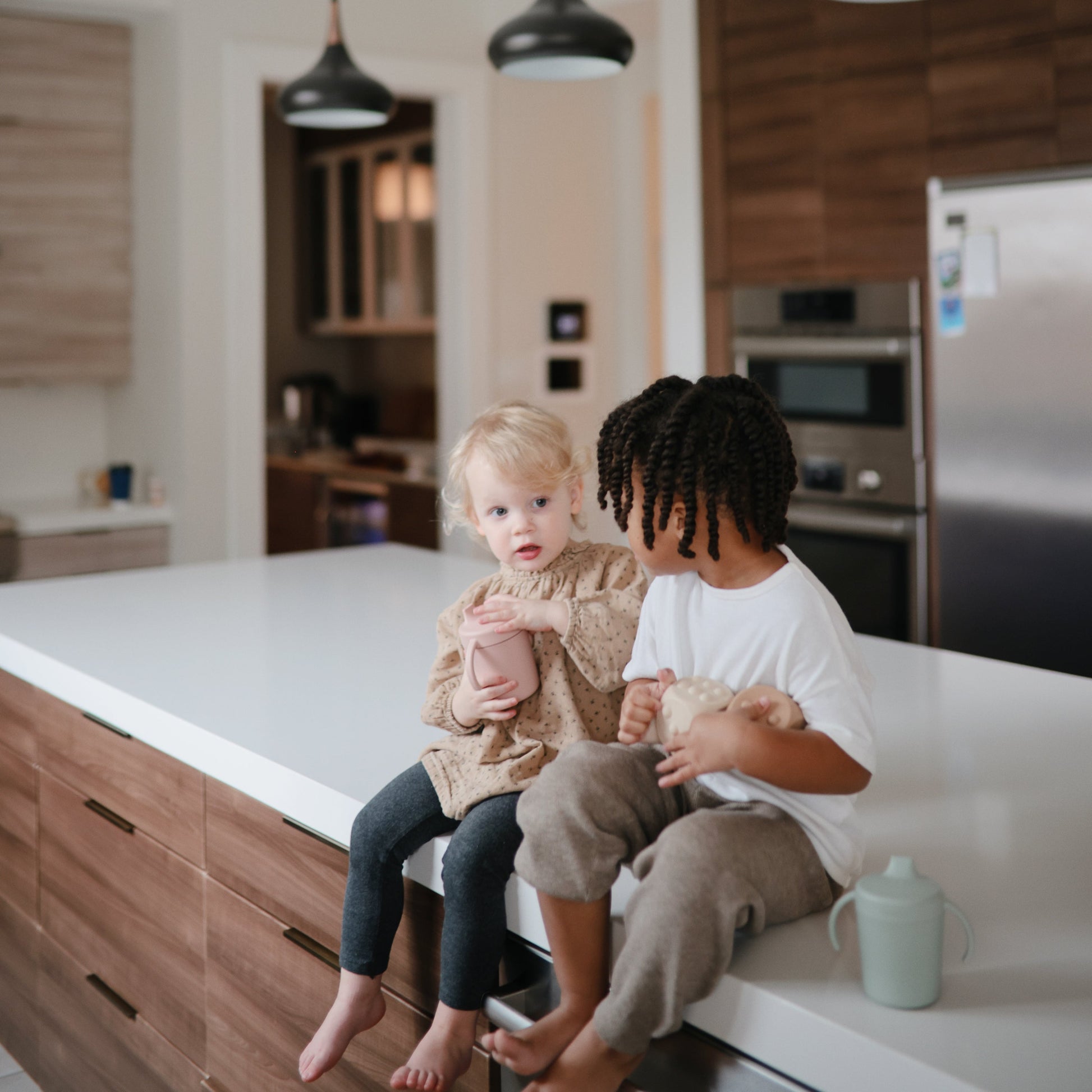 Two children sitting on a kitchen counter in a modern kitchen.