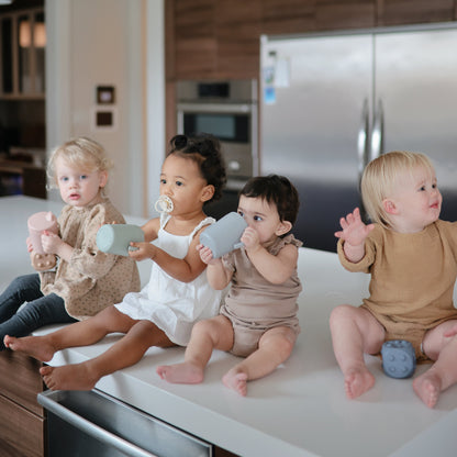 Four toddlers sitting on a kitchen counter with toys, surrounded by kitchen appliances.