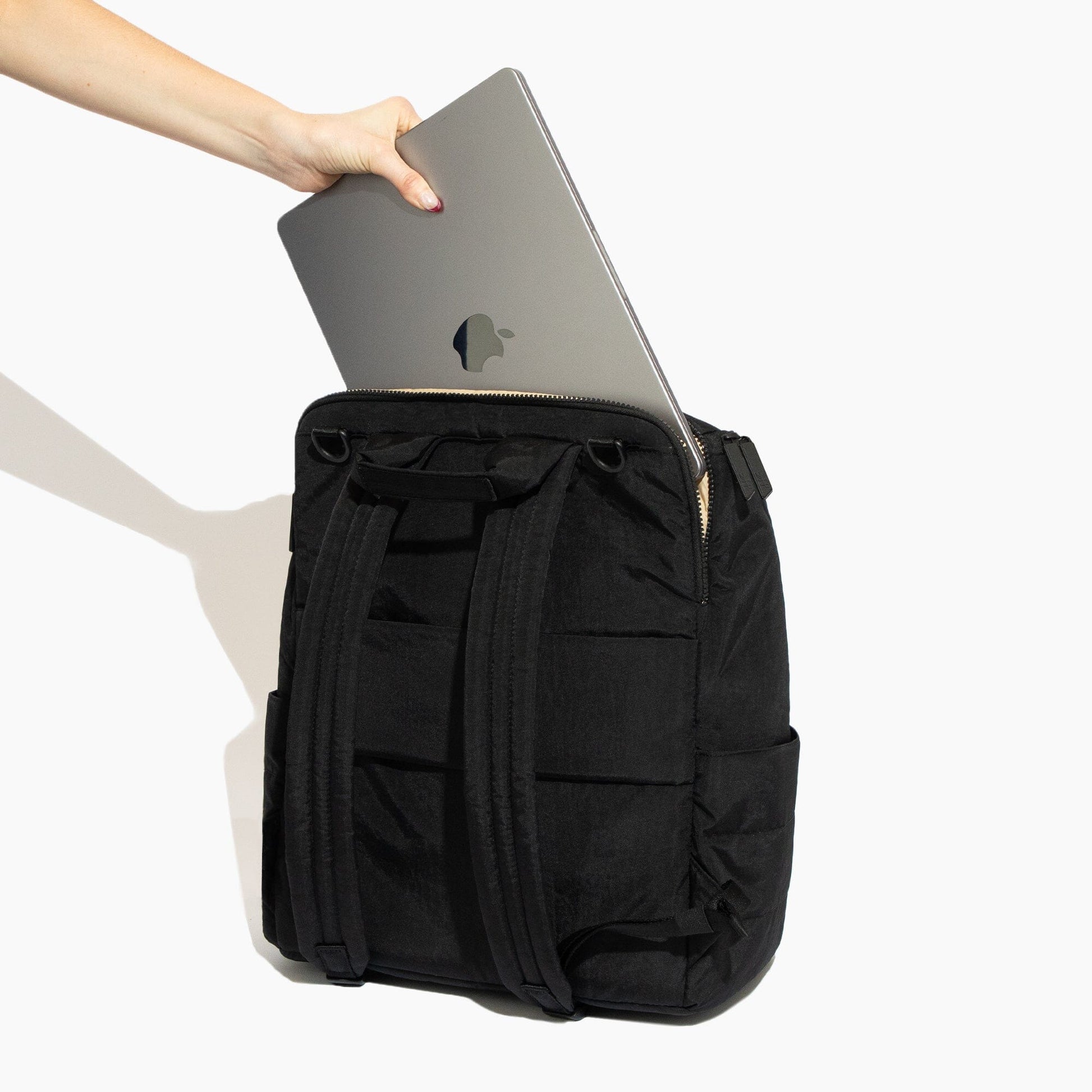 Black backpack with a laptop being placed into it on a white background