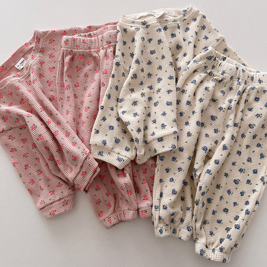 Two pairs of baby bloomers, one pink and one white with blue floral pattern, on a light gray background.