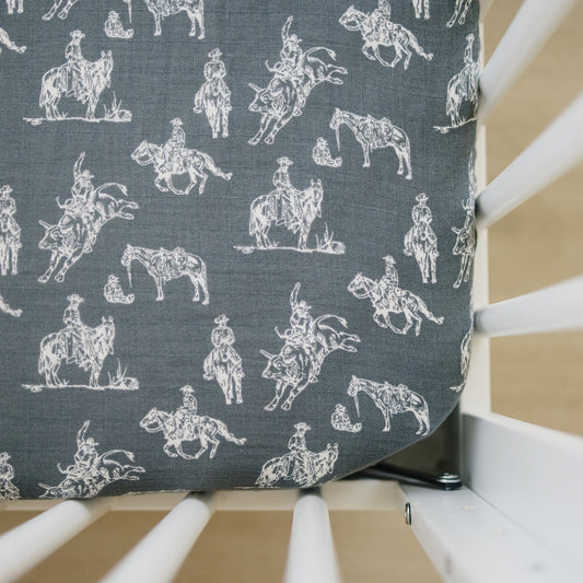 Fabric with white cowboy and horse pattern on a gray background, displayed on a chair.