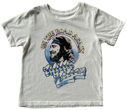 A white t-shirt with a graphic print of a male figure and the text 'On the Road Again' in a stylized font.