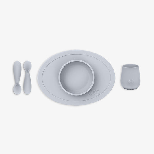Set of gray children's tableware including a bowl, plate, cup, and two spoons on a white background.