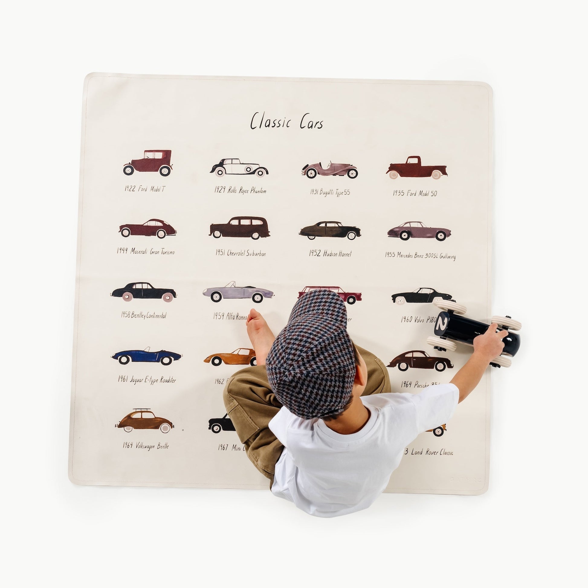 Child playing with a toy car on a 'Classic Cars' educational mat.