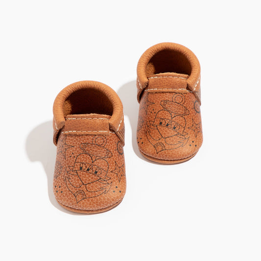 Pair of brown leather baby shoes with embossed designs on a white background