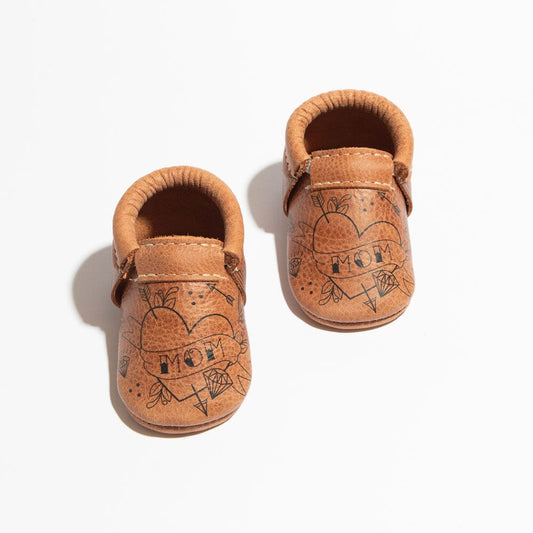 Pair of brown baby moccasins with heart designs on a white background