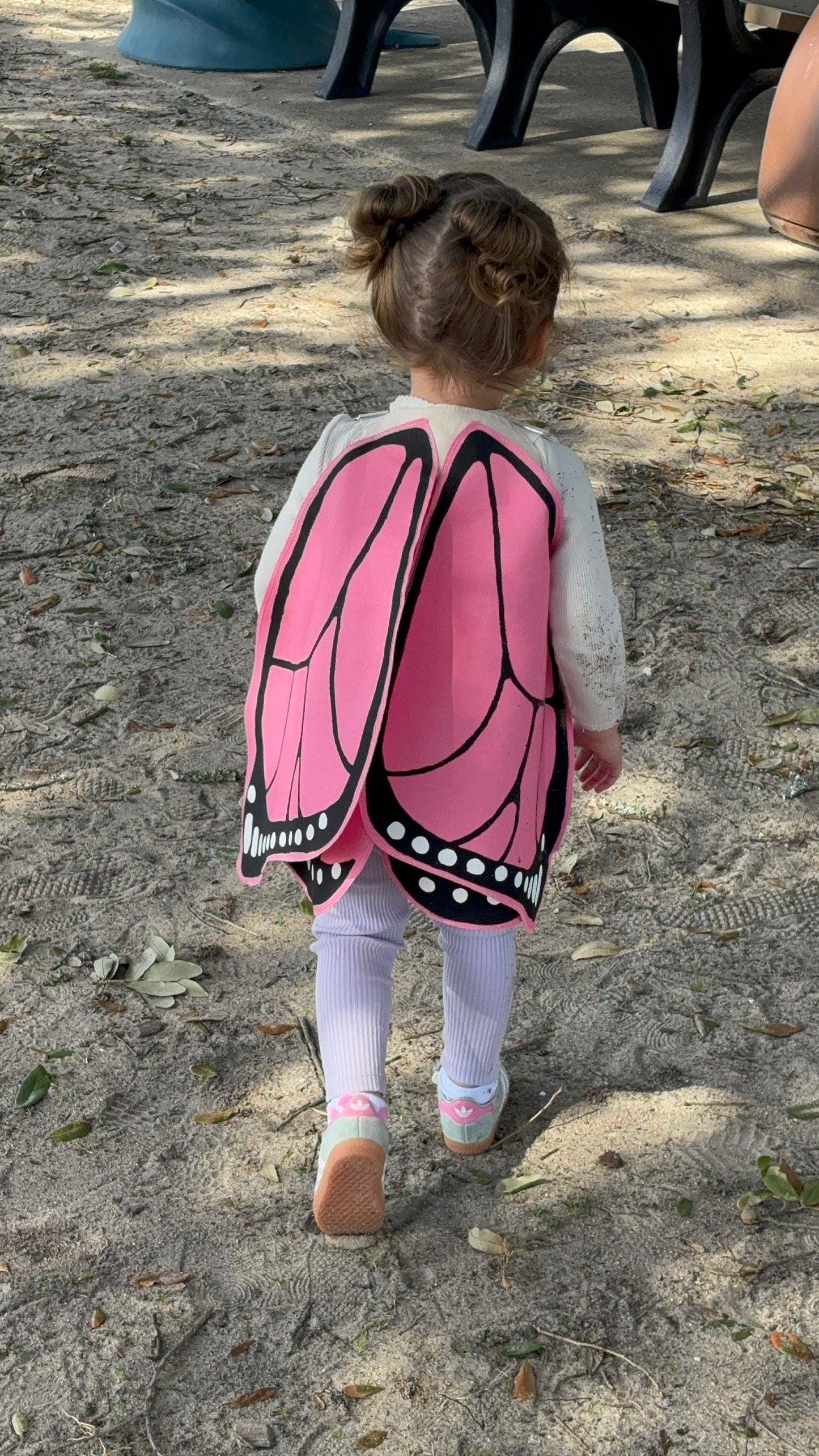 Child wearing a butterfly costume with pink wings on a sandy ground.