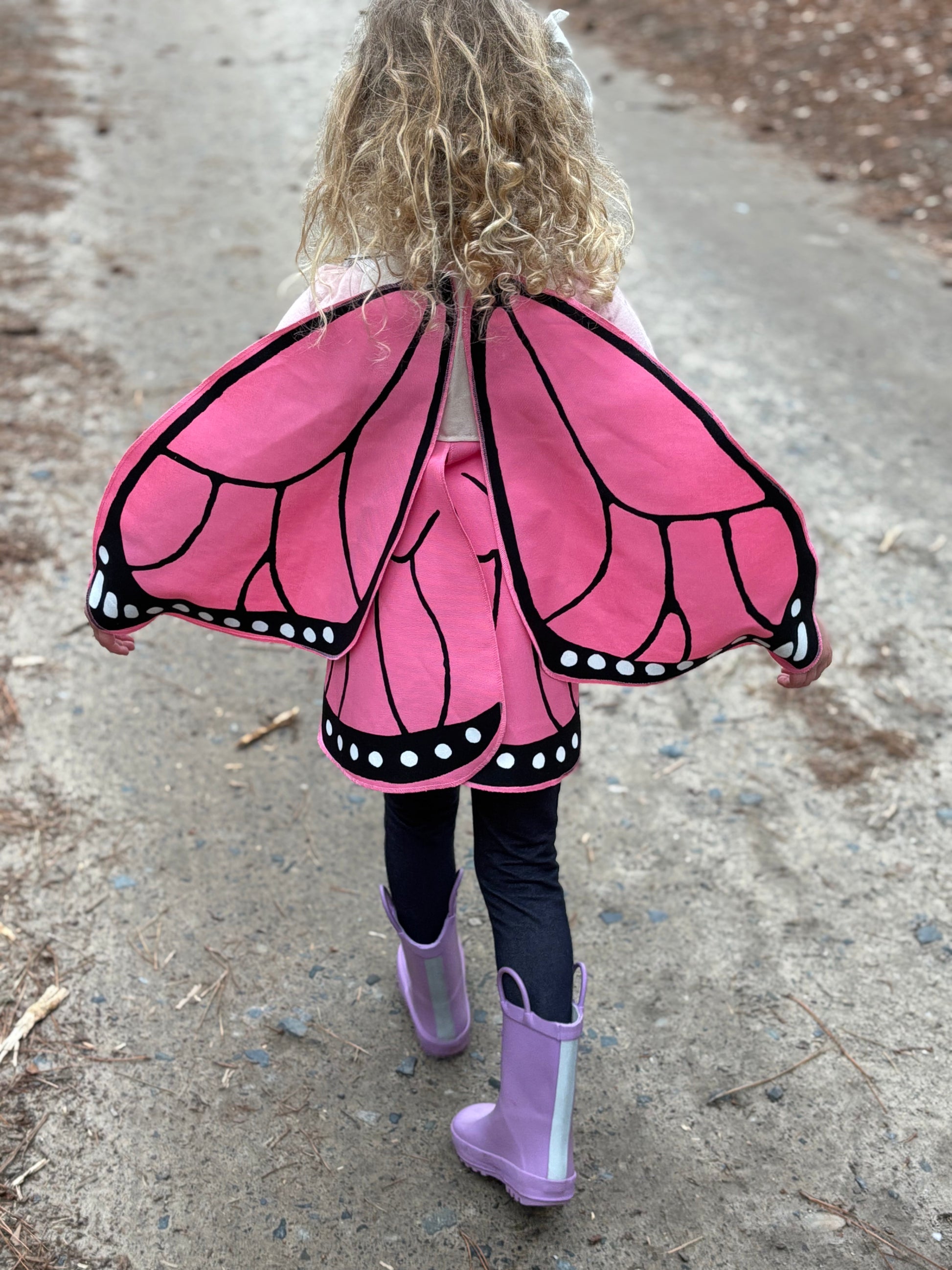 Child wearing a pink butterfly costume with black details on a concrete surface.