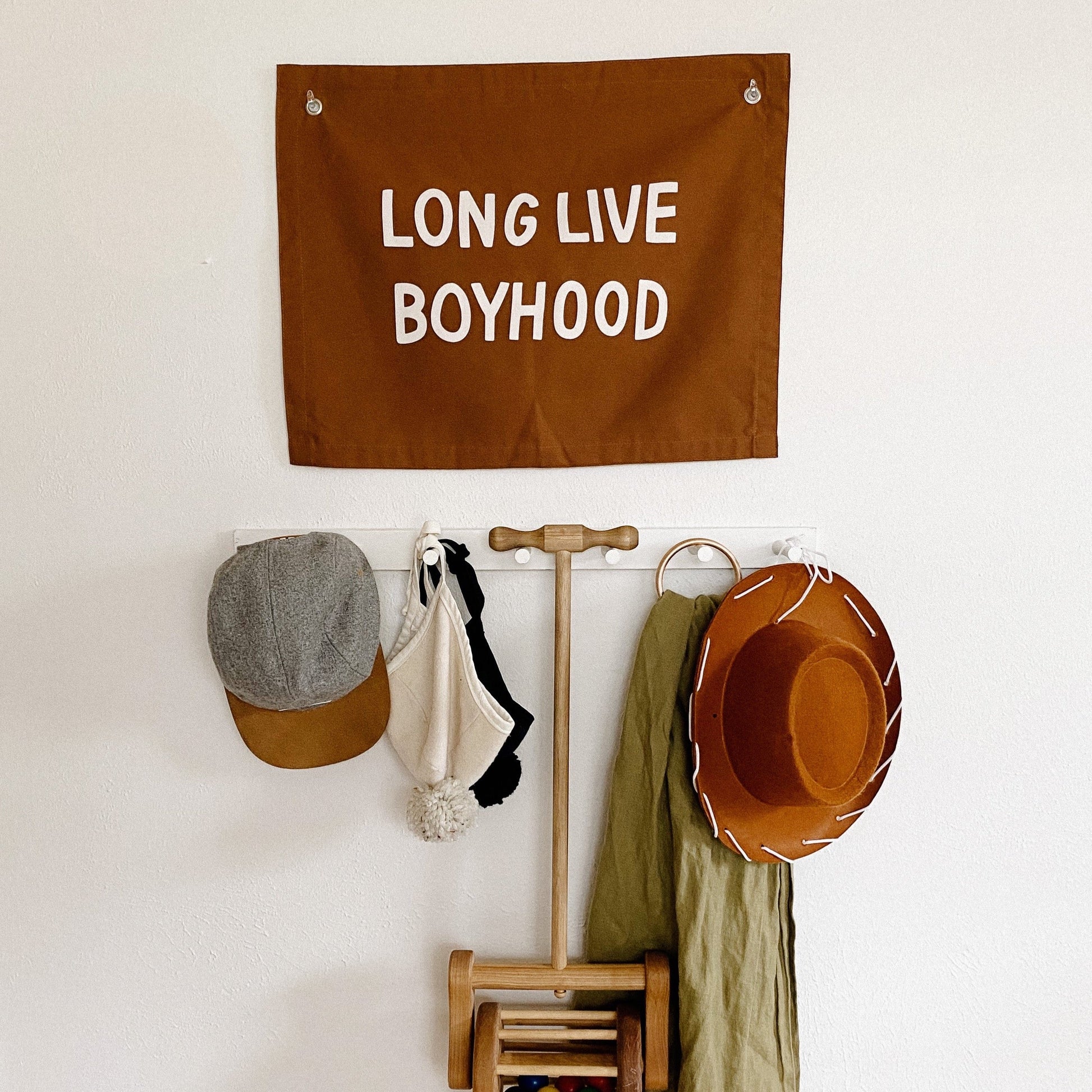 Decorative banner with 'LONG LIVE BOYHOOD' text hanging above a wall-mounted coat rack with various items.